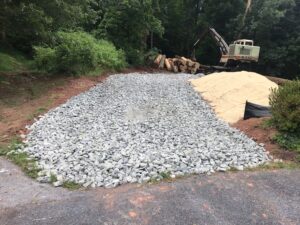 a construction site with a pile of gravel, sand, logs , and a Barko machine in the background